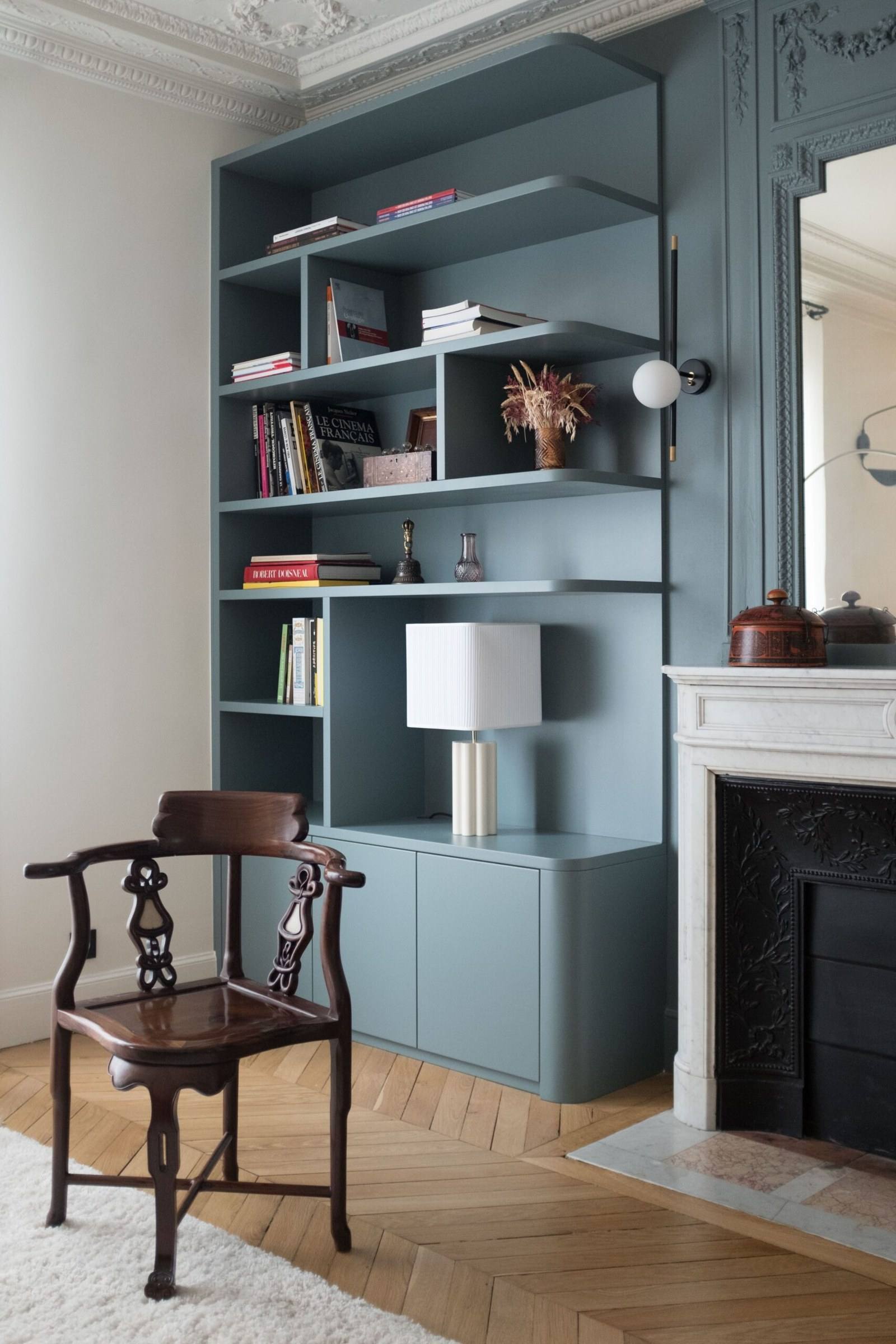 Bibliothèque bleu gris encastrée près d'une cheminée en marbre, dans un salon haussmannien