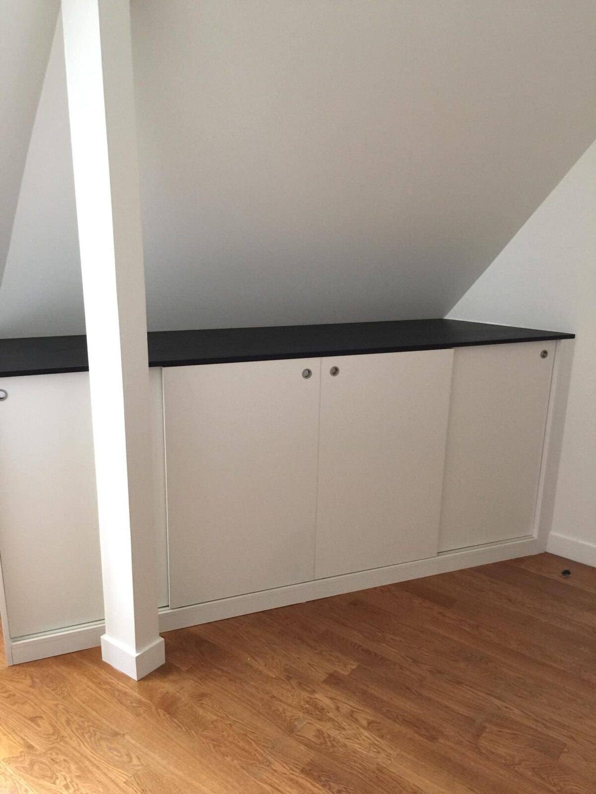 Meuble bas sous pente blanc avec plan noir, entre deux poteaux
