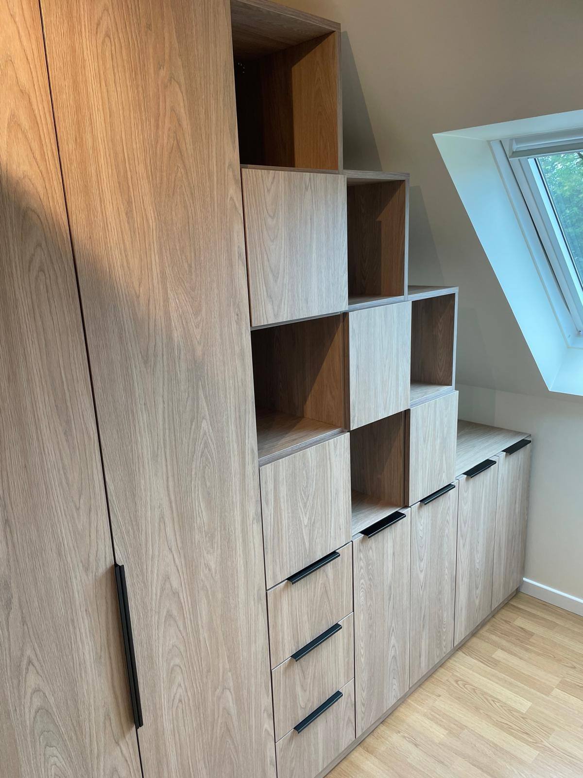 Meuble sous pente en bois clair sous fenêtre de toit, avec tiroirs et niches, à Pierrelaye