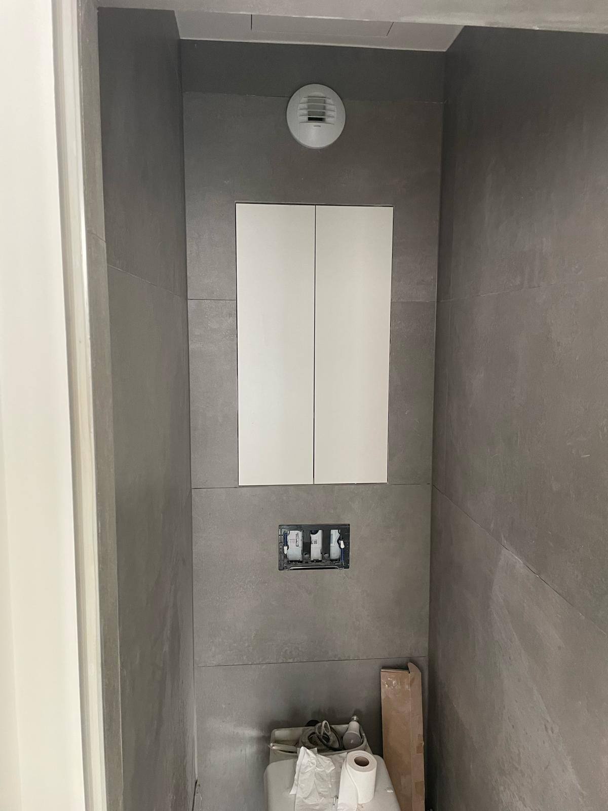 Placard encastré blanc au-dessus des toilettes, portes fermées, dans une salle d'eau à Beauchamp