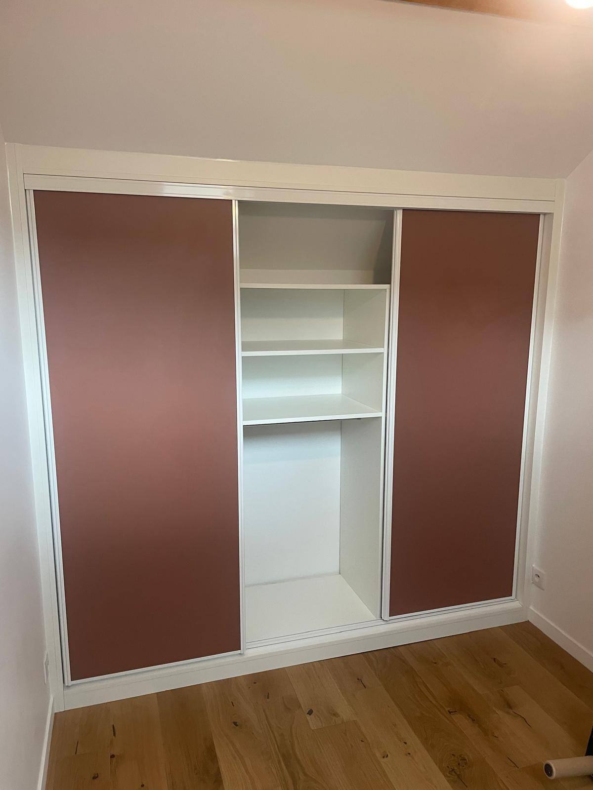 Placard de chambre à portes coulissantes vieux rose, ouvert sur des étagères blanches, à Montreuil